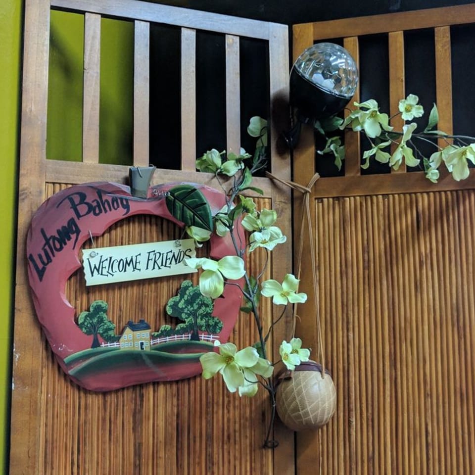 A wooden apple-shaped sign with "Lutong Bahay Welcome Friends" hangs on a bamboo wall.